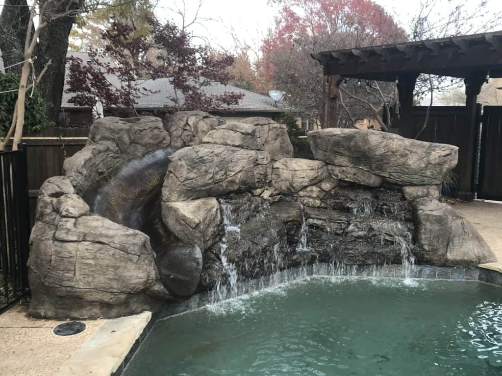 Pools come in all shapes and sizes and waterfalls do as well. This waterfall seems as though it is a weeping wall with a steady & calming trickle recycling into the pool. Arlington, TX